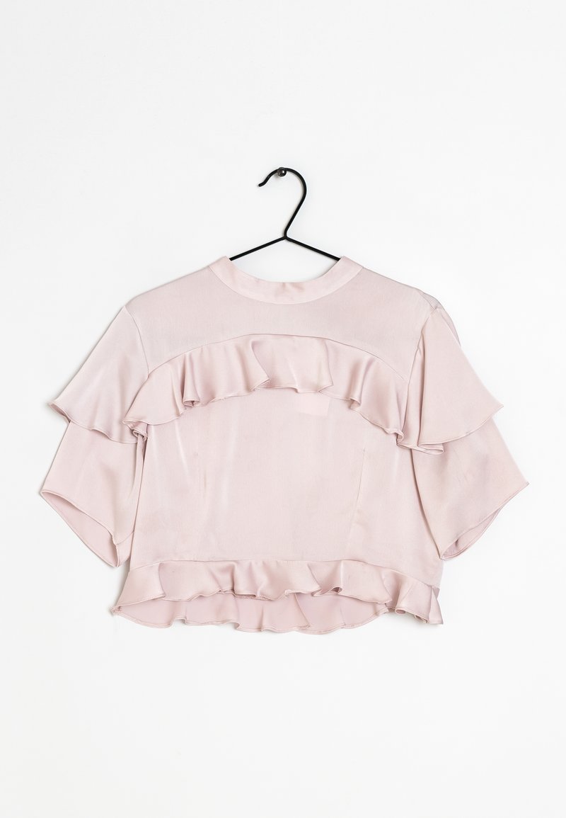 Chemisier rose avec des accents froncés, manches courtes et col rond. Confectionné en tissu lisse, accroché sur un crochet noir contre un fond blanc.