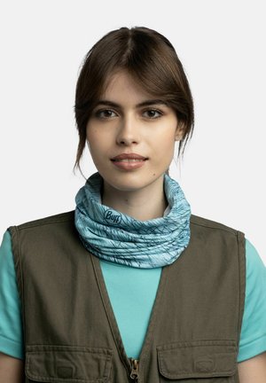Young woman with brown hair wears turquoise patterned neck gaiter, teal shirt, and olive green zippered vest, facing forward with neutral expression.