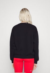 Sudadera negra de corte relajado y cuello redondo, con puños y dobladillo acanalados, combinada con pantalones cortos de ciclismo rojos.
