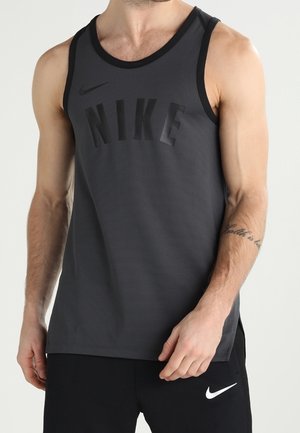 Mężczyzna ubrany w ciemnoszary bezrękawnik Nike i czarne krótkie spodenki Nike, stoi z jedną ręką przy talii.