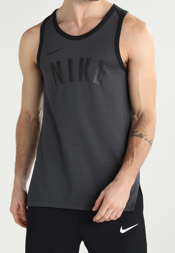 Homme portant un débardeur Nike gris foncé et un short Nike noir, debout avec une main près de sa taille.