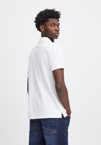 Vit polo med krage, korta ärmar och sidslitsar. Matchad med mörkblå denimjeans. Slät textur och avslappnad design.