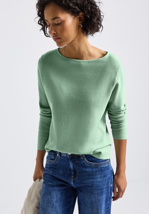 Pull en maille vert clair avec un décolleté bateau et des manches trois-quarts, associé à un jean bleu. Design simple et décontracté.