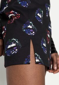 Närbild av svart kjol med sidoklyfta, dekorerad med färgglada läppmönster i blå, lila, röda och gröna blommönster.