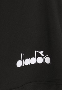 Tela negra con una textura suave que presenta el logo blanco "diadora" posicionado en el costado. Diseño simple, sin patrones o detalles adicionales.