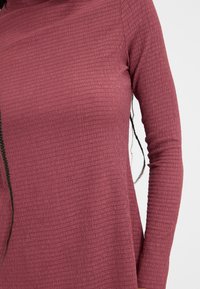 Långärmad topp i texturerad, ribbad vinröd tyg, med hög hals och en figurnära silhuett.