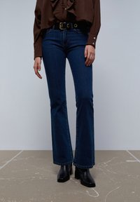 Slidseje blå denimjeans med en mørk vask, der har en klassisk pasform og er parret med et sort bæltet og ankelstøvler.