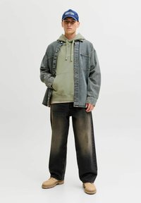 Farkkutakki päällä vaaleanvihreä huppari, yhdistettynä löysiin mustiin farkkuihin ja beigekenkäisiin. Sininen lippalakki logokiinnityksellä. Yksinkertainen, rento ilme.