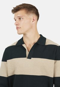 Męski sweter z ciemnozielonymi i beżowymi poziomymi pasami, bez kołnierza, o dzianinowej fakturze i wyraźnym dekolcie w serek.