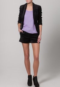 Black velvet blazer over a light purple top with a textured pattern, paired with black shorts and ankle boots. Clean, tailored lines.