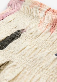 Tissu crème texturé avec de doux plis, présentant des motifs abstraits rose et vert. Comprend un détail élastiqué froncé en haut.