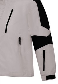 Giacca leggera grigia con accenti neri; presenta tasche con zip e un design slanciato e inclinato sulle maniche. Texture liscia e resistente all'acqua.