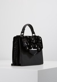 Czarna torebka na ramię z kwiatowymi zdobieniami na klapie, łańcuszkowym paskiem i trójkątnym okuciem. Wykonana ze skóry o gładkiej fakturze.