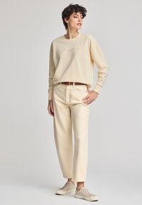 Felpa beige chiaro con logo "Polo Club", abbinata a jeans beige a gamba dritta. Indossata con sneakers beige. Texture liscia.