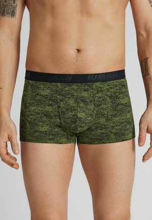 Mannelijke torso met groene boxershorts met camouflagemotief, zwarte tailleband en zichtbare tatoeages op de armen.