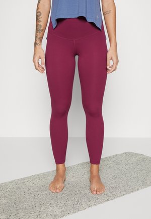 Leggings bordeaux avec une texture lisse et une taille haute, assortis à un haut de sport bleu ample. Les pieds sont nus sur une surface grise.
