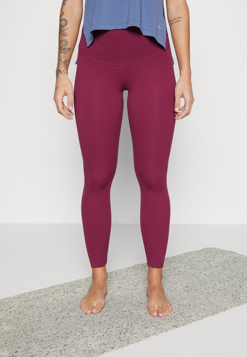 Leggings burdeos con una textura suave y una cinturilla alta, combinados con una camiseta deportiva azul holgada. Los pies están descalzos sobre una superficie gris.