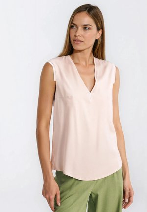 Jasnoróżowa bluzka z krótkim rękawem, dekoltem w kształcie litery V i subtelnym połyskiem; zestawiona z zielonymi, luźnymi spodniami z fakturowanej tkaniny.