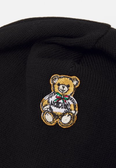 Căciulă tricotată neagră, având un patch brodat cu un urs în culorile galben și alb, purtând o panglică verde și roșie, cu textul "Mochino".