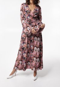 Kukkaruusuinen mekko vaaleanpunaisena, jossa mustia, violetteja ja sinisiä kuvioita. Pitkät kellosovituiset hihat ja virtaava siluetti, yhdistettynä valkoisiin korkokenkiin.