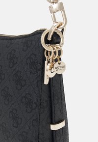 Czarna torebka o fakturowanej powierzchni z paskiem na złotym łańcuszku, zdobiona logo i zamykana na zamek błyskawiczny z brelokami.