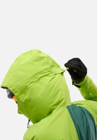 Veste imperméable verte avec des accents noirs et une capuche ; comprend un cordon de serrage ajustable et un col haut pour une protection contre le vent.