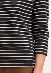 Czarny i biały pasiasty top z długim rękawem, wykonany z miękkiego materiału, z równymi poziomymi paskami i luźnym fasonem w pasie.