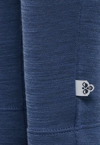 Marinblå textil med en fin stickad struktur, med en liten vit etikett med en logotyp på sidan. Tyget är slätt och tätt vävt.