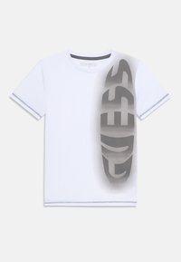 Vit bomullströja med en stor grå "GUESS"-logotyp tryckt diagonalt. Sömdetaljer i ljusgrått vid ärmarna och halsringningen.
