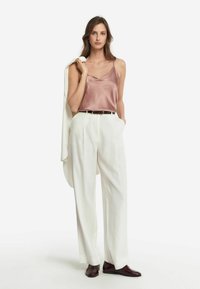 Satinrosa linne med tunna axelband, parat med högmidjade vita byxor. Accessoarer med ett mörkt bälte och vinröda skor.