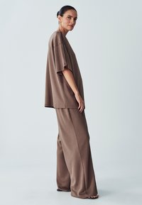 Brown relaxed-fit top with dropped shoulders paired with matching wide-leg pants. Smooth texture, minimalist design, and no visible patterns.