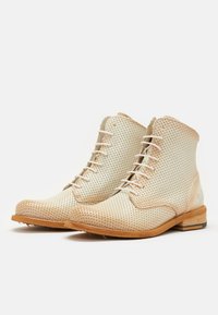 Botas de tobillo de cuero perforado beige con cordones blancos, punta redondeada y tacones de madera marrón. Diseño minimalista con sutiles detalles de costura.