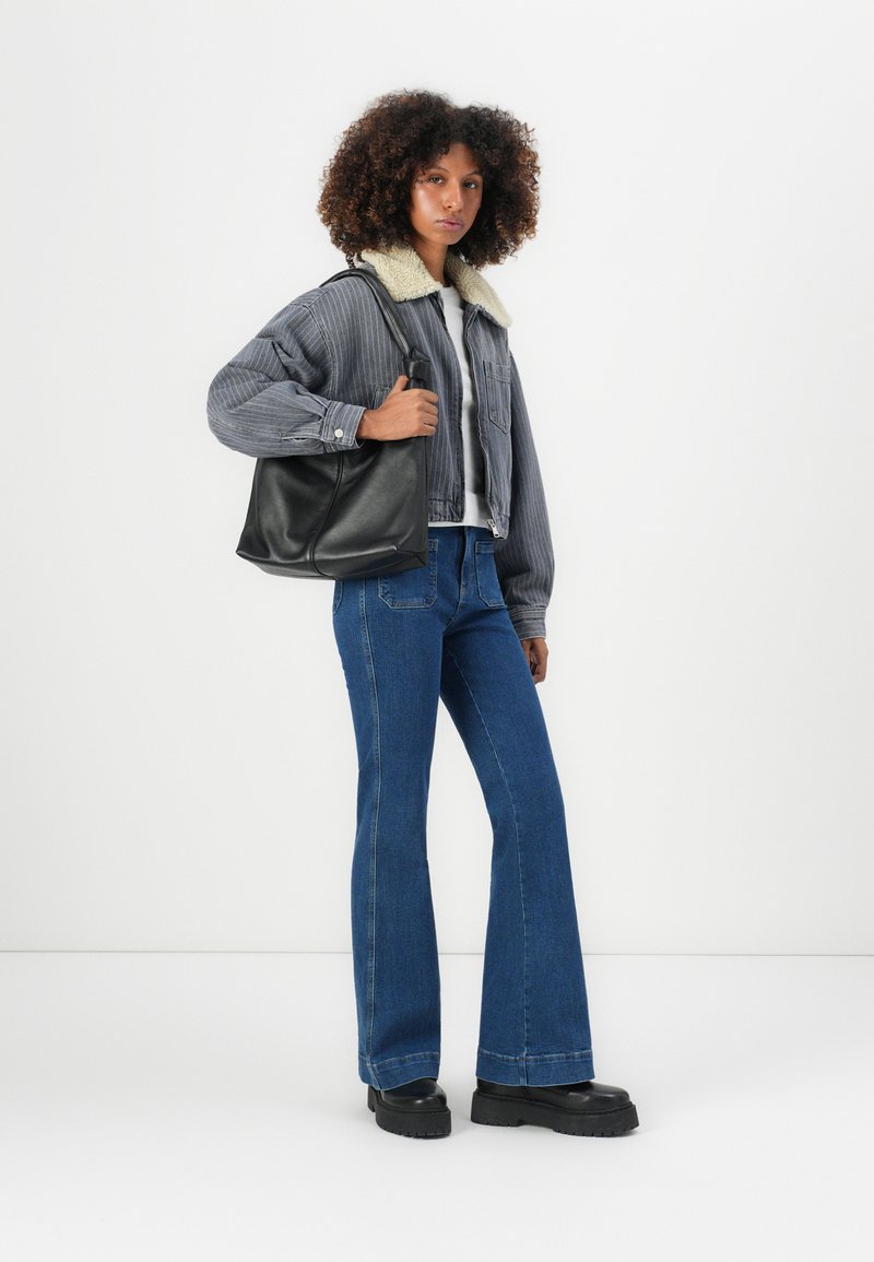 Schwarze Lederhandtasche, graue Cordjacke mit Schaffellkragen, weißes Hemd, blaue Schlagjeans und klobige schwarze Plateaustiefel.