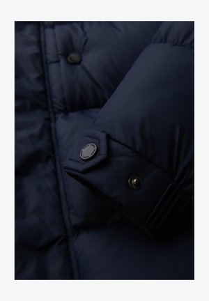 Chaqueta acolchada de color azul marino con diseño acolchado, textura suave y botones de presión de plástico negro en las mangas y en el frente.