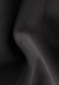 Tessuto nero con una consistenza morbida e liscia, caratterizzato da un motivo a maglia fine e una leggera caduta. Illuminato delicatamente per mettere in risalto profondità e dettagli.