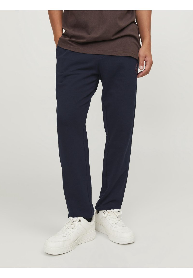 Navy blue sweatpants gjorda av en bomullsblandning; har en avslappnad passform, elastisk midja och en liten logotyp på vänster sida.