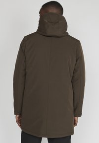 Parka căldură maro cu o croială dreaptă și o textură moale. Prezintă un design fără cusături și buzunare ascunse, potrivit pentru vreme mai rece.