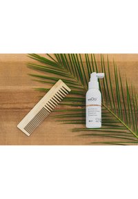 Bamboe kam met brede en smalle tanden naast een witte spuitfles met oranje accenten, rustend op een houten oppervlak en palmblaadjes.