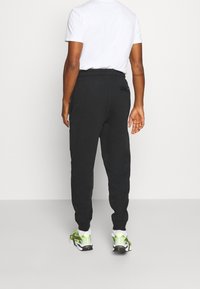 Schwarze Jogginghose mit elastischem Bund und Seitentaschen, mit schmal zulaufendem Bein. Kombiniert mit weißem T-Shirt und bunten Sneakern.