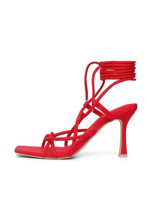 Rote High-Heel-Sandaletten mit dünnen, überkreuzten Riemen und einem gewickelten Knöcheldesign. Glatte Oberfläche mit einer quadratischen Zehenpartie und beiger Sohle.