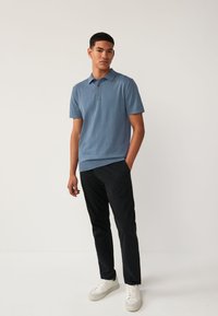 Polo in morbido tessuto blu chiaro, con maniche corte e patta con tre bottoni. Abbinato a pantaloni neri e sneakers bianche. Texture liscia.