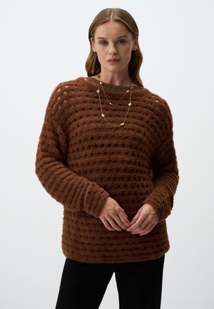 Maglione marrone con una vestibilità ampia, caratterizzato da un motivo a pois, collo a costine e maniche lunghe. Accompagnato da una collana d'oro a strati.