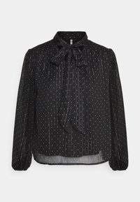 Blusa nera con maniche lunghe, caratterizzata da un nastro al collo. Il tessuto presenta pois bianchi e righe verticali, creando un dettaglio texture.