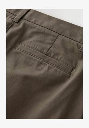 Rudos kelnės iš lygaus, tekstūruoto audinio. Yra užpakalinis kišenė su tvarkingu, tiesiu siūlė ir be matomų detalių ar puošmenų.