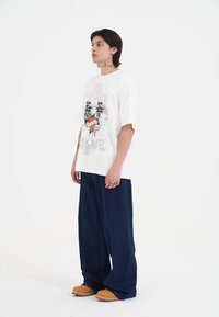 T-shirt bianco con design grafico, jeans larghi blu scuro e zoccoli color sabbia. Linee semplici, vestibilità comoda ed elementi grafici notevoli.