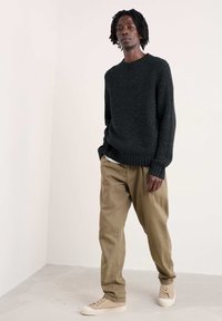 Crna točkasta džemper s rebrastim izrezom i manžetama, u kombinaciji s laganim kašmirastim hlačama opuštenog kroja i bež niskim tenisicama.