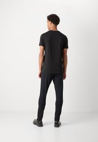 T-Shirt scurt negru din bumbac. Purtați-l cu pantaloni închiși, strâmți și încălțăminte neagră. Design simplu și minimalist, fără modele vizibile.