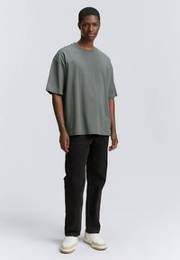 Prevelika siva majica s kratkimi rokavi, kombinirana s črnimi hlačami in belimi supergami z bež poudarki. Gladek teksturni material.