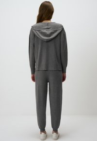 Hoodie gris avec cordon de serrage et coupe décontractée, associé à un pantalon de jogging assorti. Tissu doux et poignets côtelés. Des baskets complètent l'ensemble.