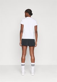 T-shirt branca de manga curta combinado com uma saia atlética preta. A modelo usa meias até ao joelho com riscas pretas e sapatilhas brancas.